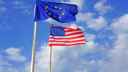 EU and US flags on flagpoles against a cloudy, blue sky
