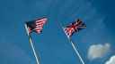 Flagpoles with flags of the US and UK fluttering in the wind, with a blue sky in the background