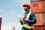 A customs worker wearing a high-viz jacket standing in front of shipping containers and carrying a clipboard with customs documentation
