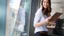 Woman holding a tablet in an office and looking out of a window